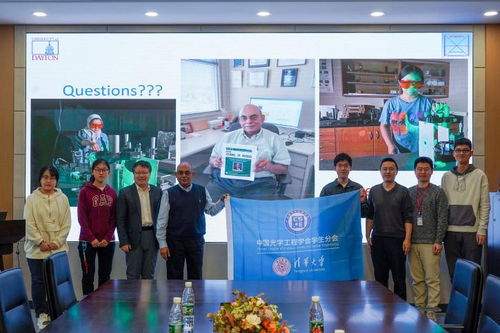 Dr. Banerjee and invited guests standing in front of a presentation slide with photos of students working in the lab