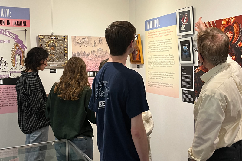 Students look at a Marian Library gallery exhibit with their professor